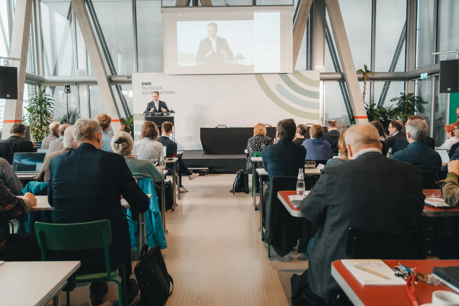 Blick in den Saal, vorne Carsten Schneider (Bundesumweltminister), der auch nochmal in groß als Bild auf der Leinwand im Hintergrund erscheint
